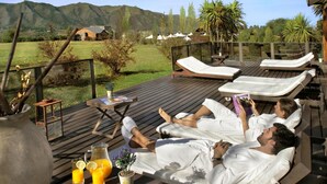 A deck with lounge chairs, a table with drinks, and a scenic mountain view. - Chamonix Posada y Spa (Villa General Belgrano)