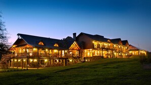A large, multi-story lodge with a prominent front porch and multiple windows, set against a twilight sky. - Chamonix Posada y Spa (Villa General Belgrano)