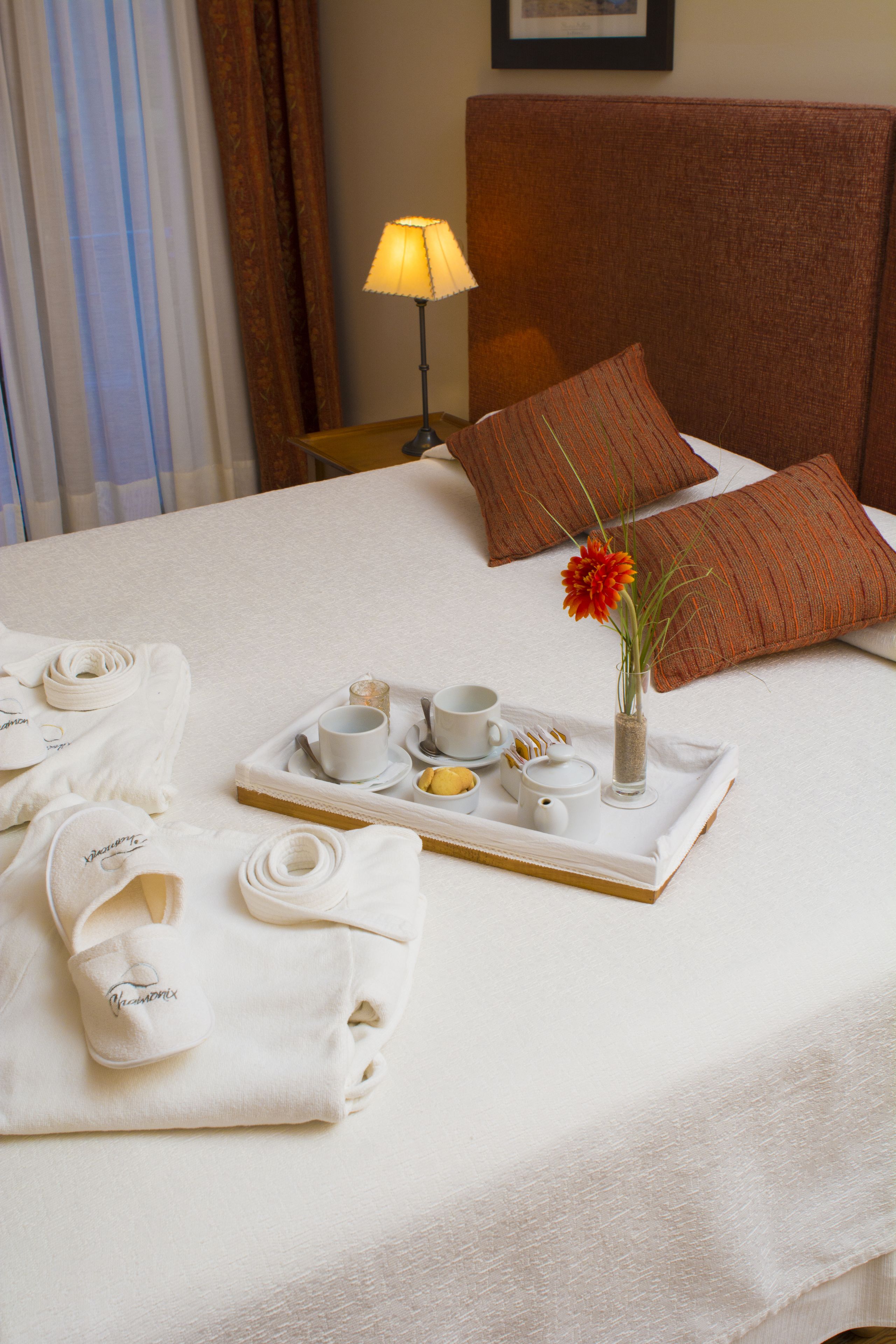 A neatly made bed with a tray of breakfast items, towels, and a vase with a flower.