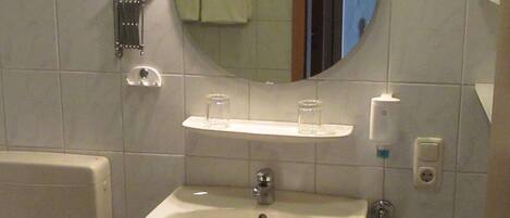 Un baño con lavamanos, espejo, toallero y dispensador de jabón.
