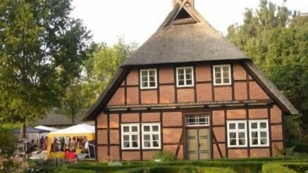 A traditional half-timbered house with a steeply pitched roof, surrounded by well-maintained gardens and trees. - Neuenkirchener Hof (Neuenkirchen)
