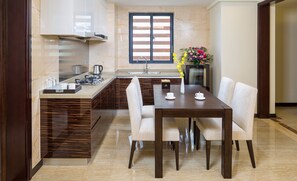 A modern kitchen with a built-in island, a dining area with a wooden table and chairs, and a large window with blinds.