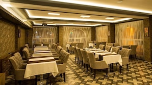 A hotel dining area with multiple tables and chairs, a patterned floor, and a ceiling with recessed lighting. - Kars-i Sirin Hotel (Kars)