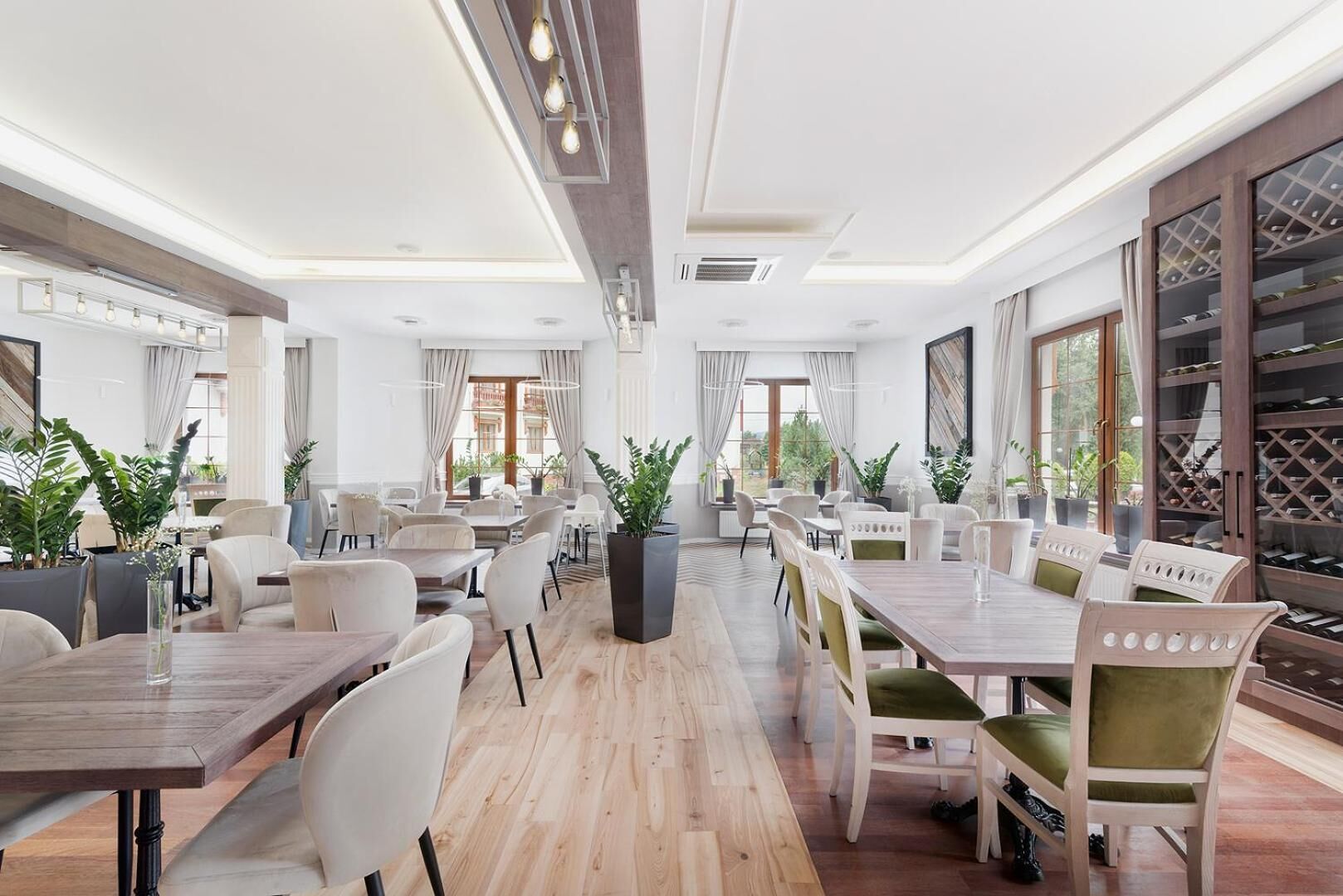 A spacious dining area with multiple tables and chairs, large windows, and potted plants.