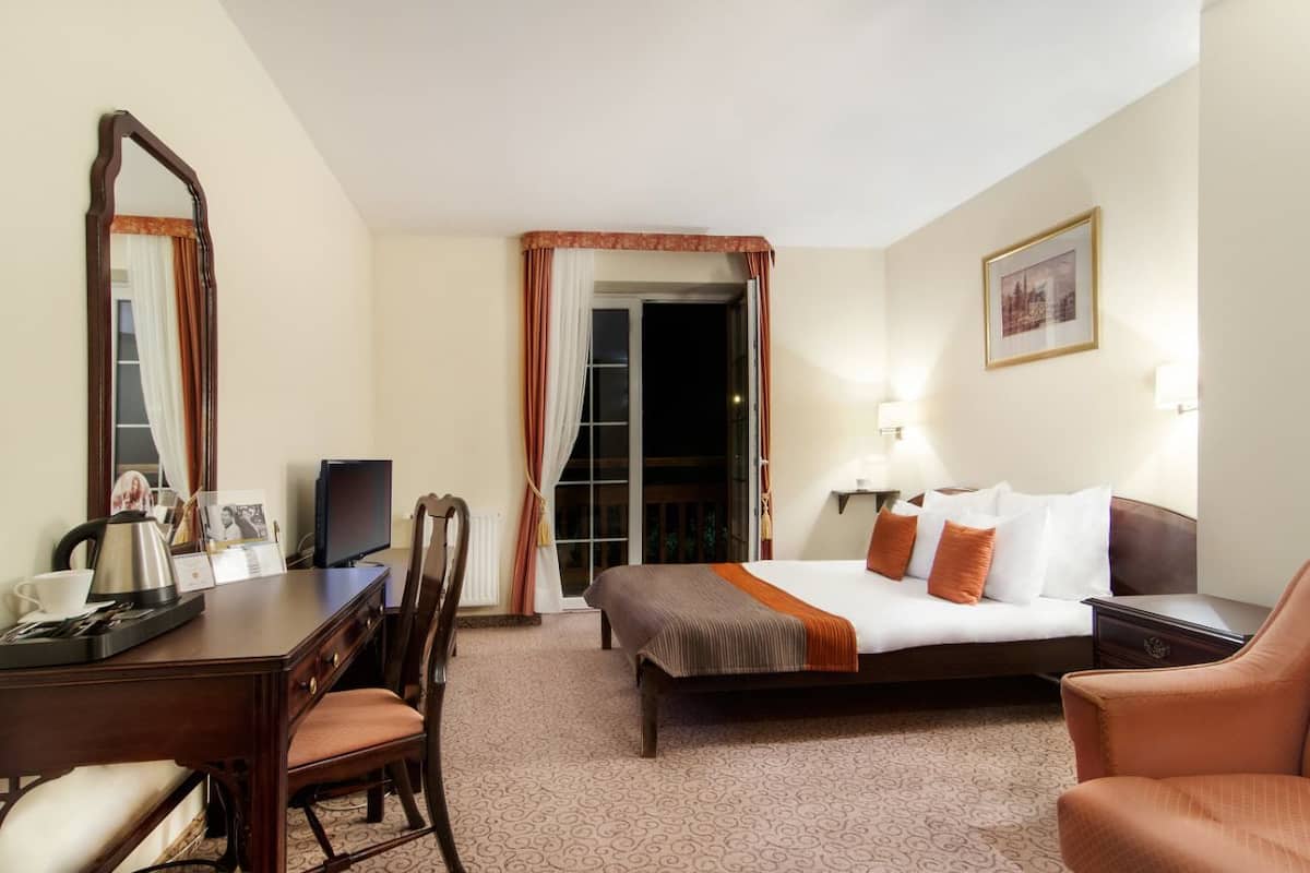 A hotel room with a bed, a desk with a chair, a television, and a large mirror.