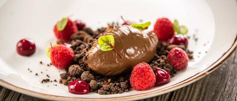 A dessert on a plate with chocolate, raspberries, and a sprig of mint.