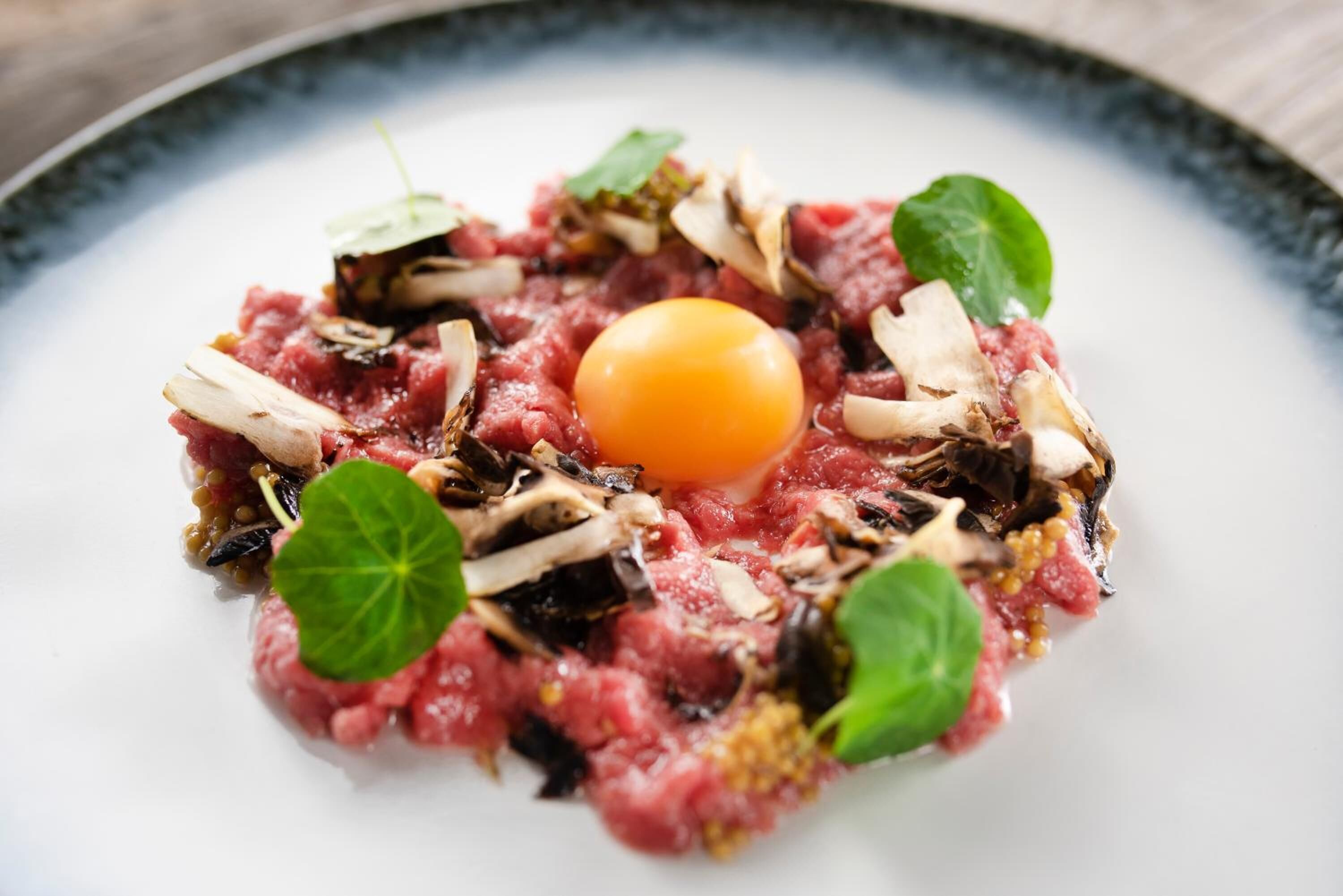 Un plato con carne cruda, hongos y una yema.