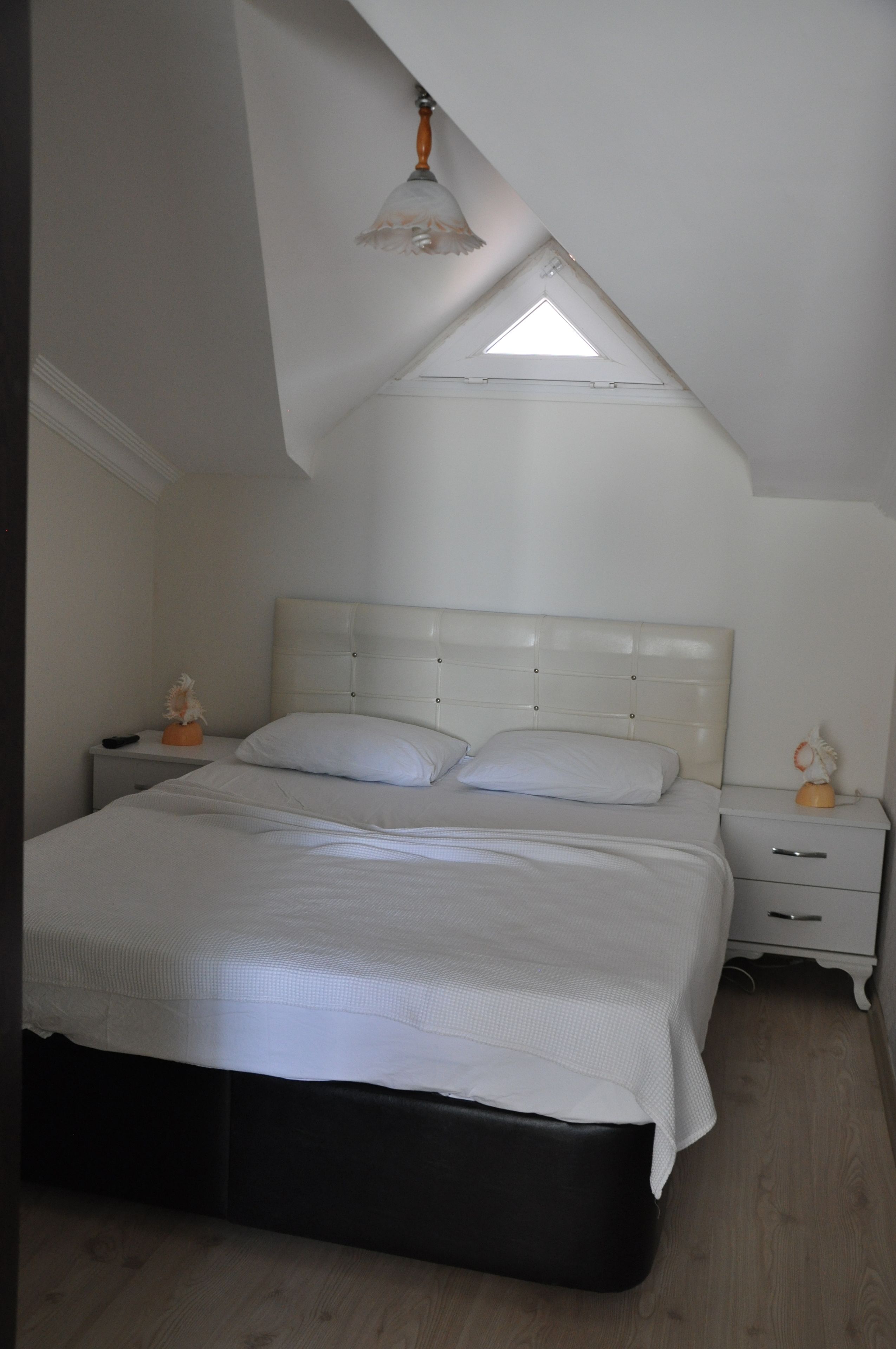 A bedroom with a bed, nightstands, a lamp, and a skylight.
