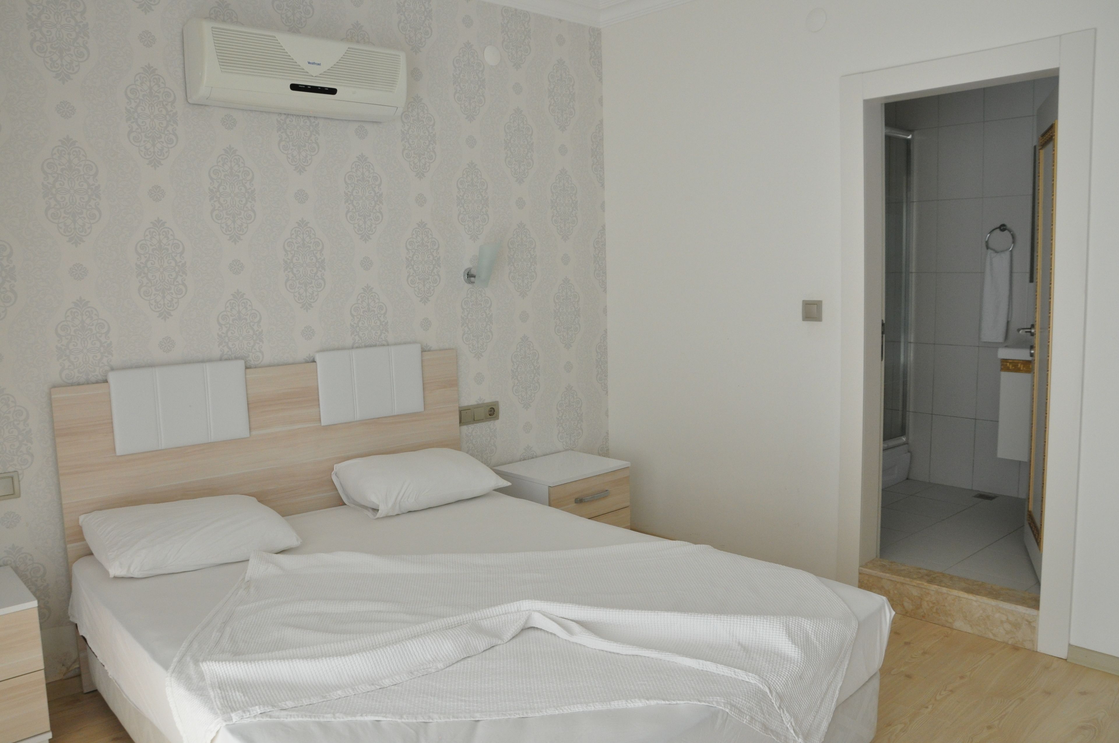A hotel room with a large bed, bedside tables, a nightstand, a mirror, and a shower area.