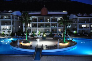 Un hotel con piscina, sillones de descanso y palmeras.