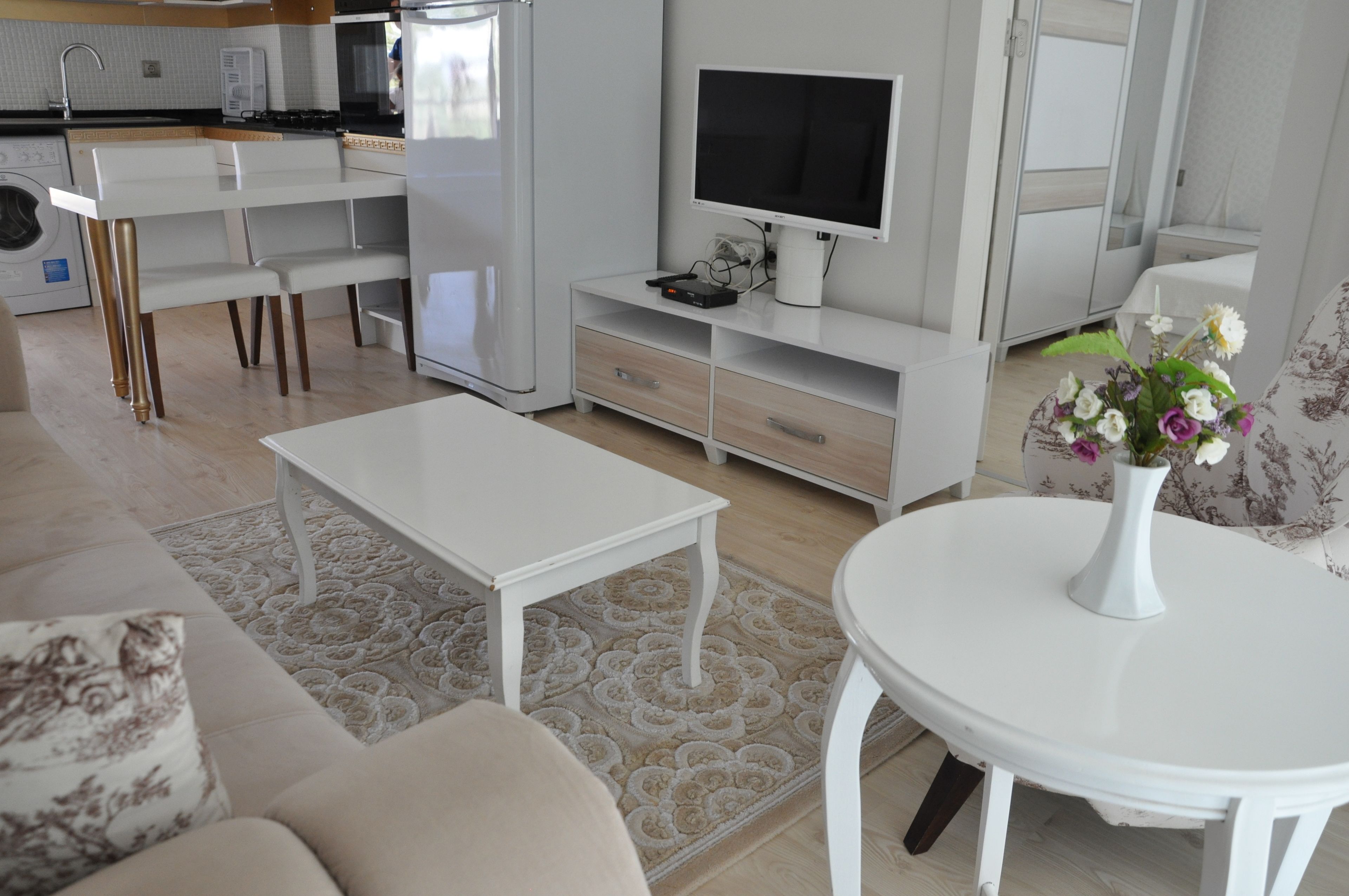 Un salon moderne avec un canapé blanc, une table basse, un téléviseur et un coin repas comprenant une table et des chaises blanches.