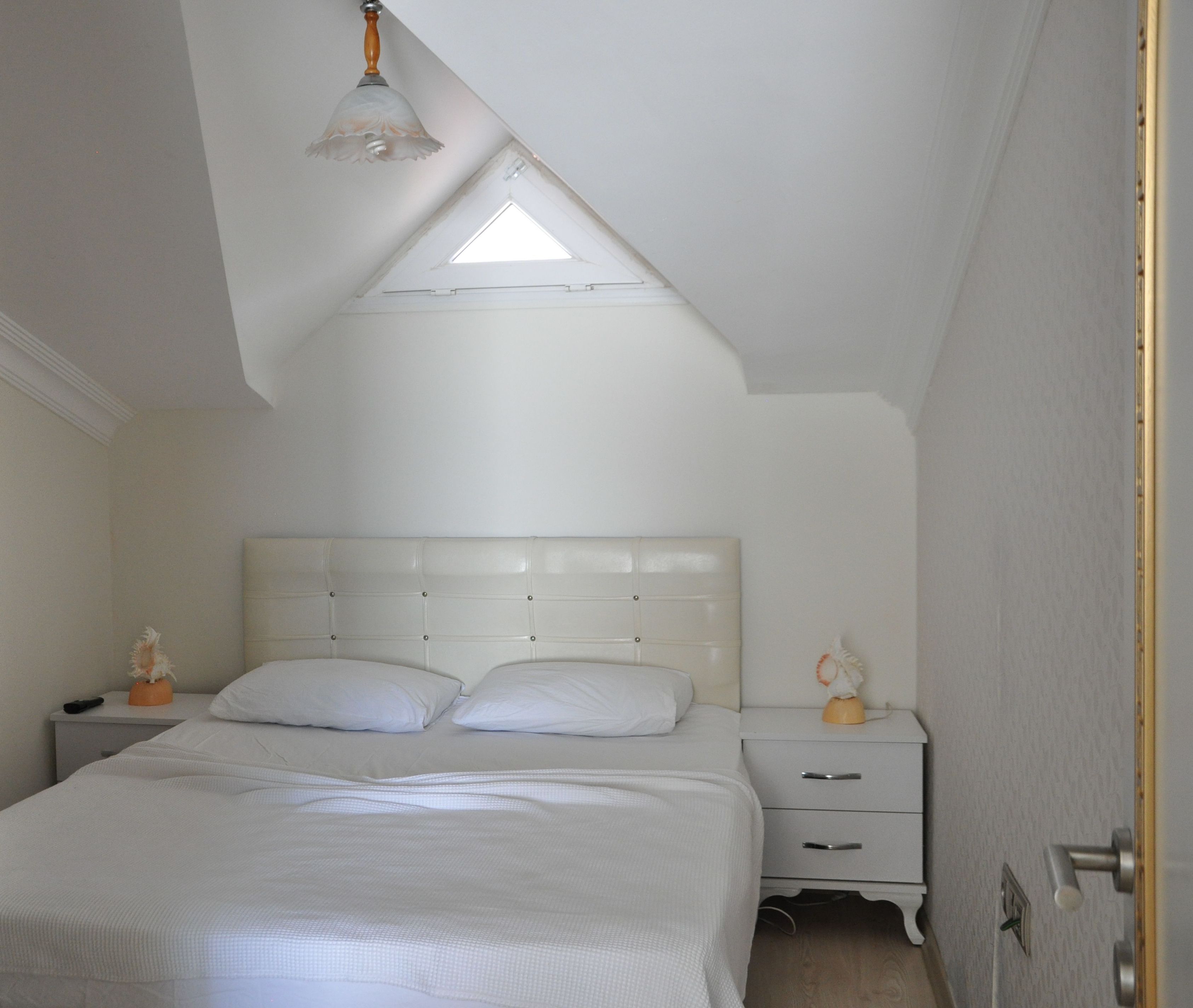 A bedroom with a white bed, a nightstand, a lamp, and a door.