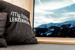 A pillow with the text "My home LENZERHEIDE" against a window with a mountain view. - Revier Mountain Lodge Lenzerheide (Vaz-Obervaz)