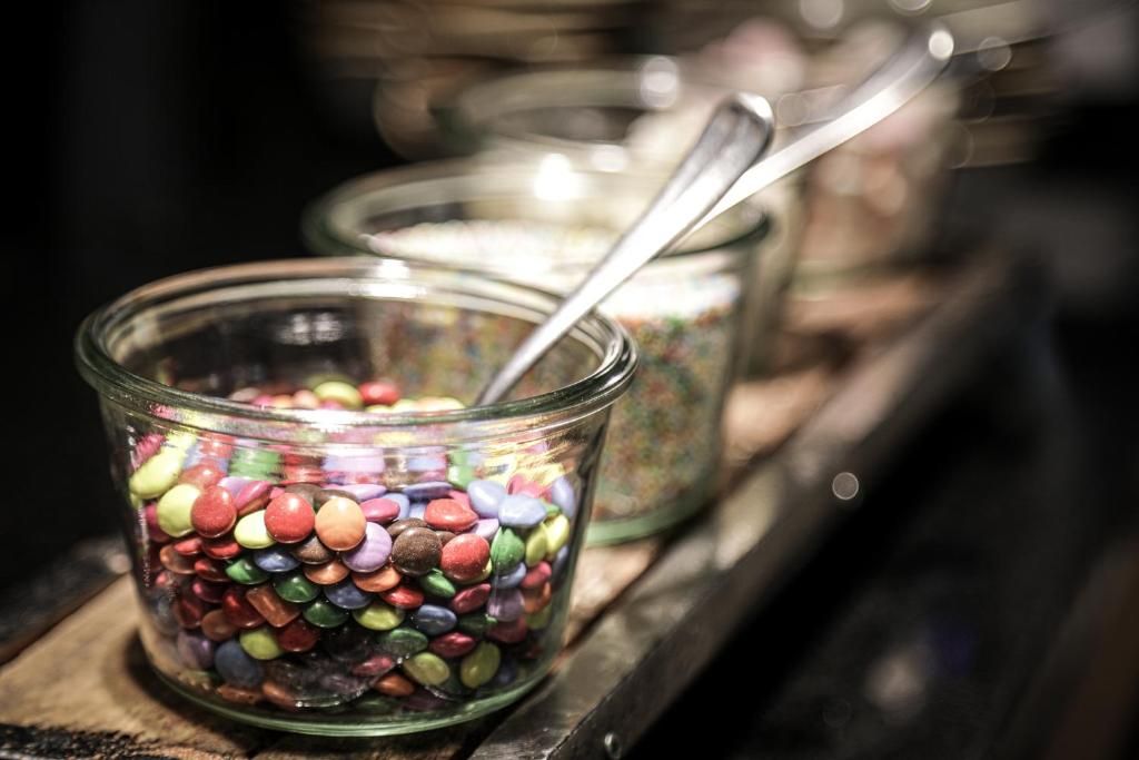 A glass jar filled with colorful candies, with a spoon inside, placed on a wooden surface.