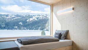 A cozy room with a large window offering a view of a snowy mountain landscape. - Revier Mountain Lodge Lenzerheide (Vaz-Obervaz)