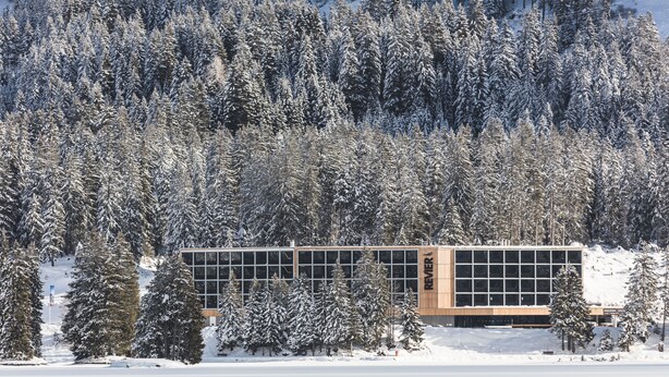 A modern building with a glass facade surrounded by snow-covered trees. - Revier Mountain Lodge Lenzerheide (Vaz-Obervaz)