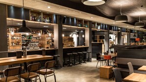 A modern bar with wooden shelves stocked with bottles, bar stools, and tables. - Revier Mountain Lodge Lenzerheide (Vaz-Obervaz)