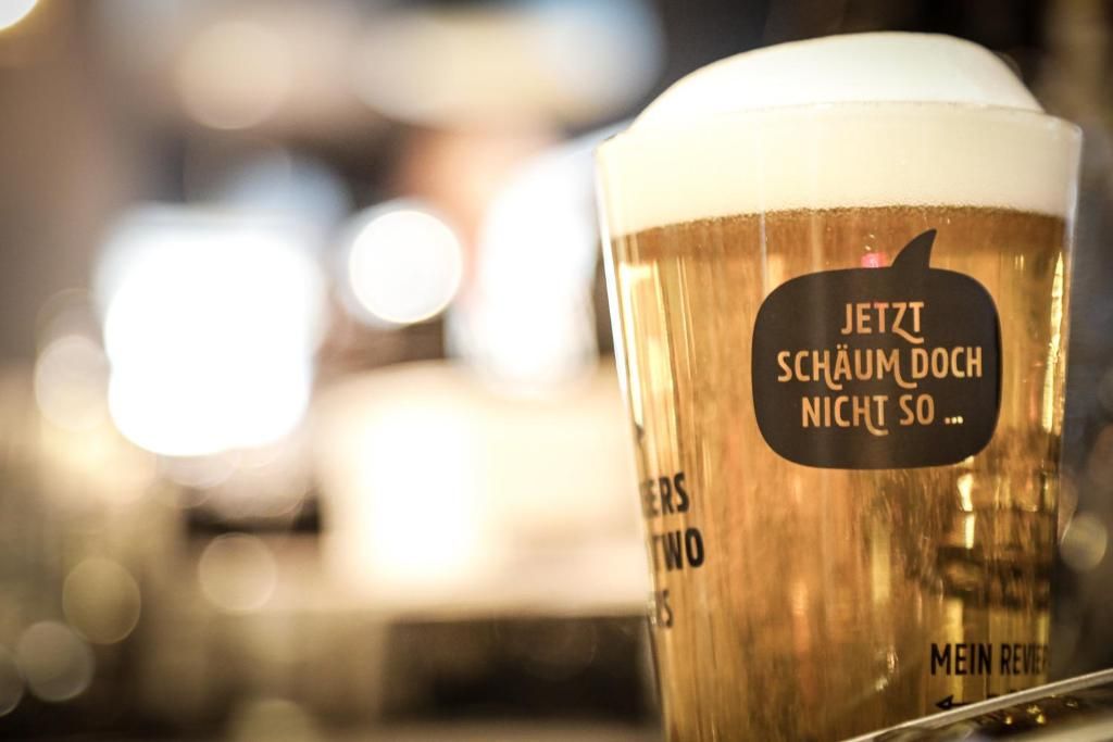 A glass of beer with a label that reads 'JETZT SCHÄUM DOCH NICHT SO...'.