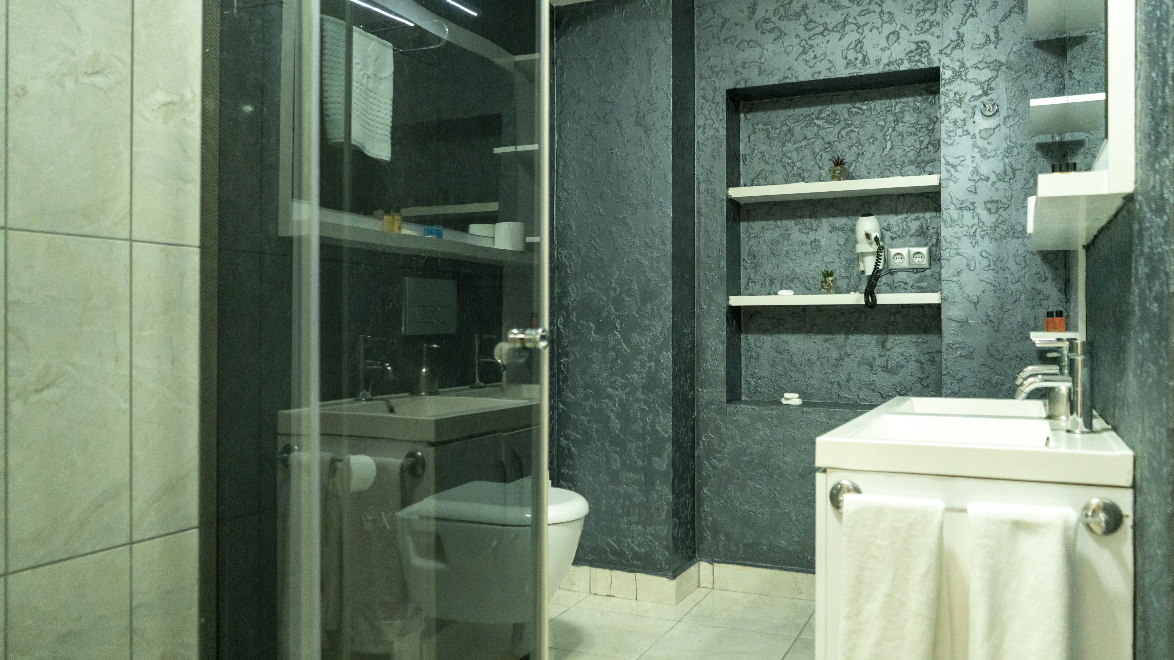 Une salle de bain moderne avec une douche à parois de verre, un lavabo blanc et un mur à motifs foncés.
