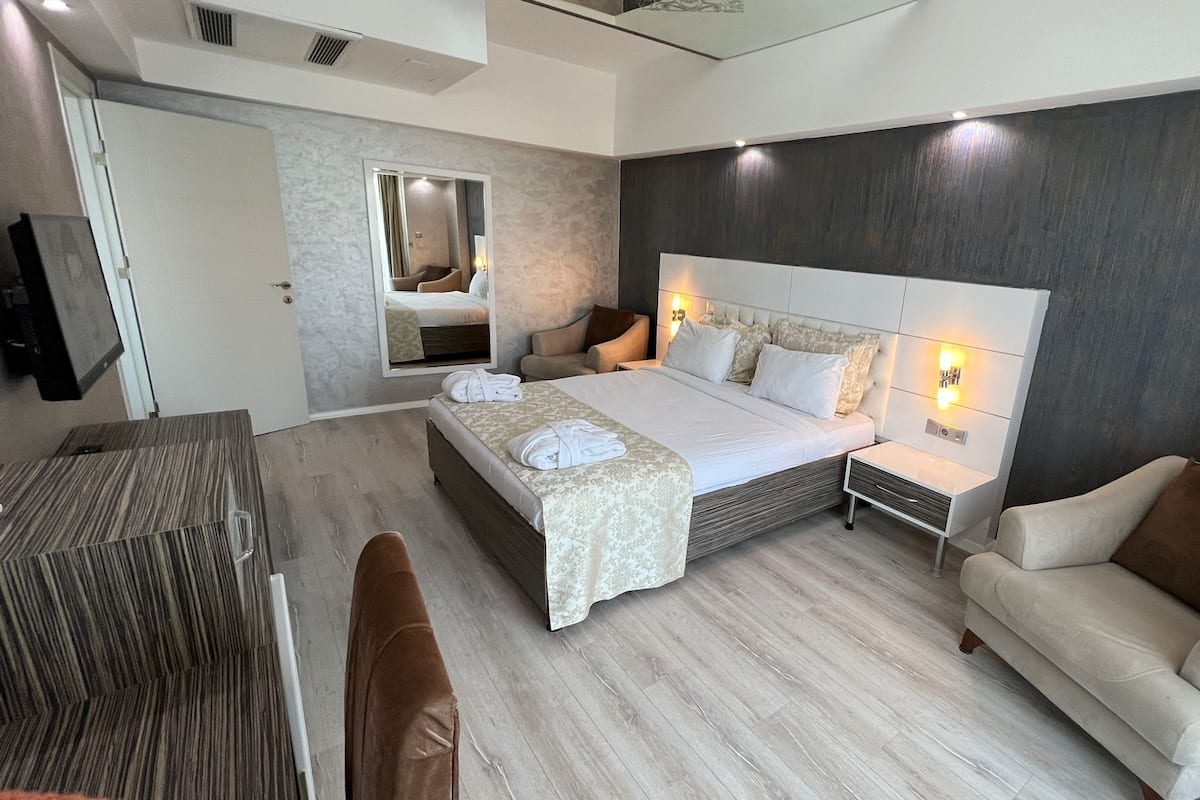Una habitación de hotel moderna con una cama grande, una zona de estar con un sofá, una mesita y un espejo.