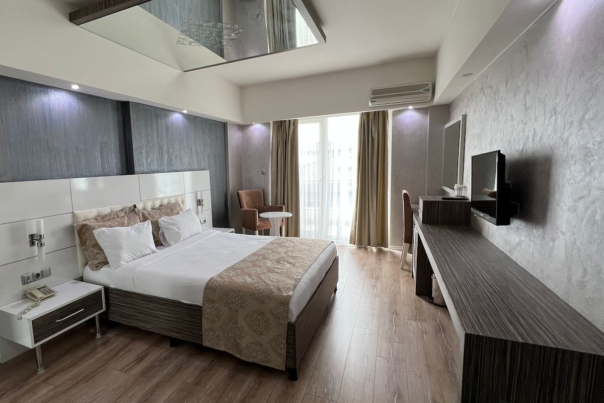 Una habitación de hotel moderna con una cama grande, mesitas de noche, un televisor y un escritorio.