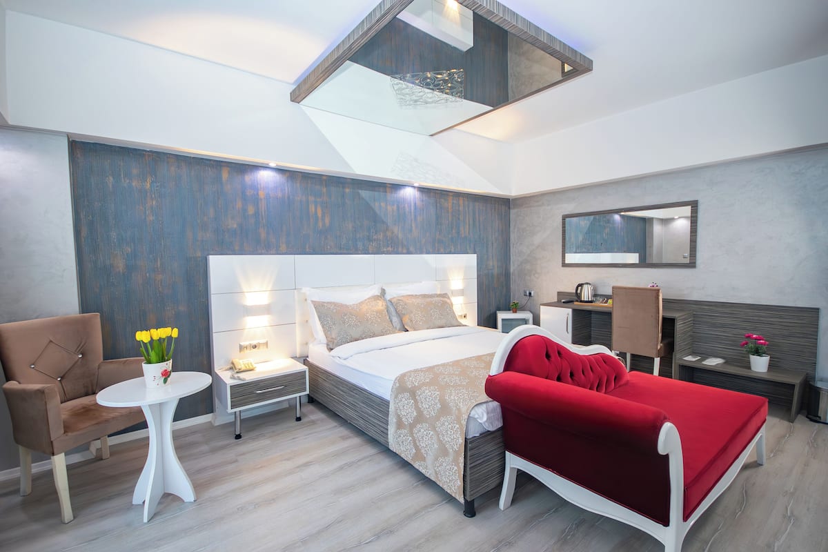 Un dormitorio moderno con una cama grande, un sofá rojo, una mesita con flores y un espejo en la pared.
