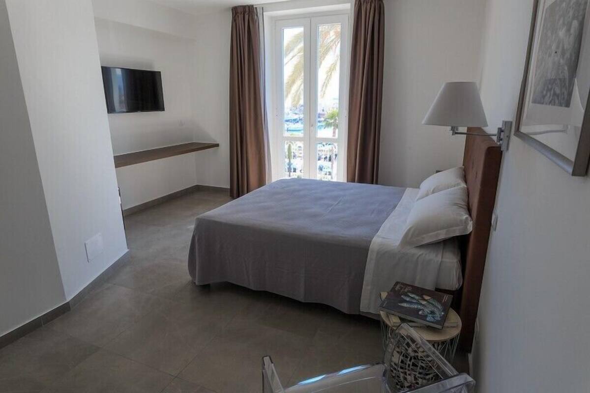A hotel room with a bed, a TV mounted on the wall, a window with curtains, and a lamp.