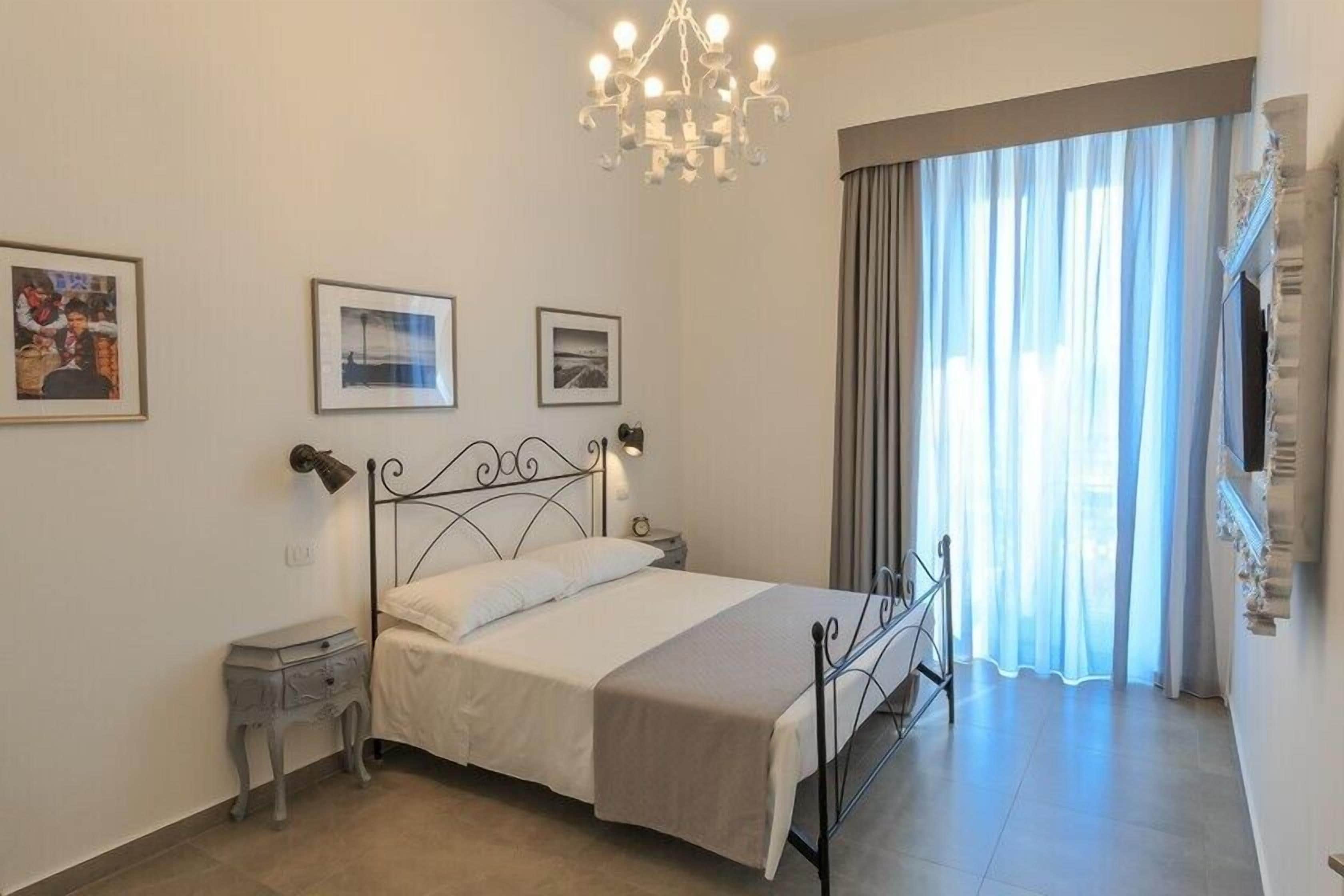 A bedroom with a bed, bedside tables, a chandelier, curtains, and framed pictures on the wall.