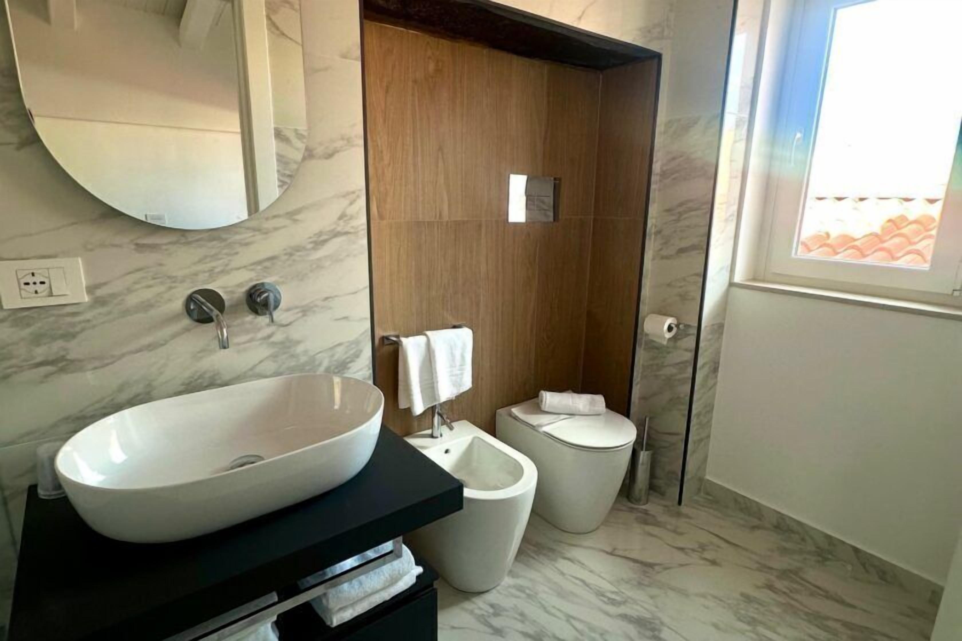 A modern bathroom with a large oval sink, a bidet, and a toilet.