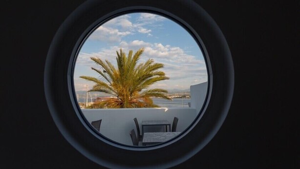 Vista circular desde una ventana mostrando una palmera y una mesa con sillas en un balcón.