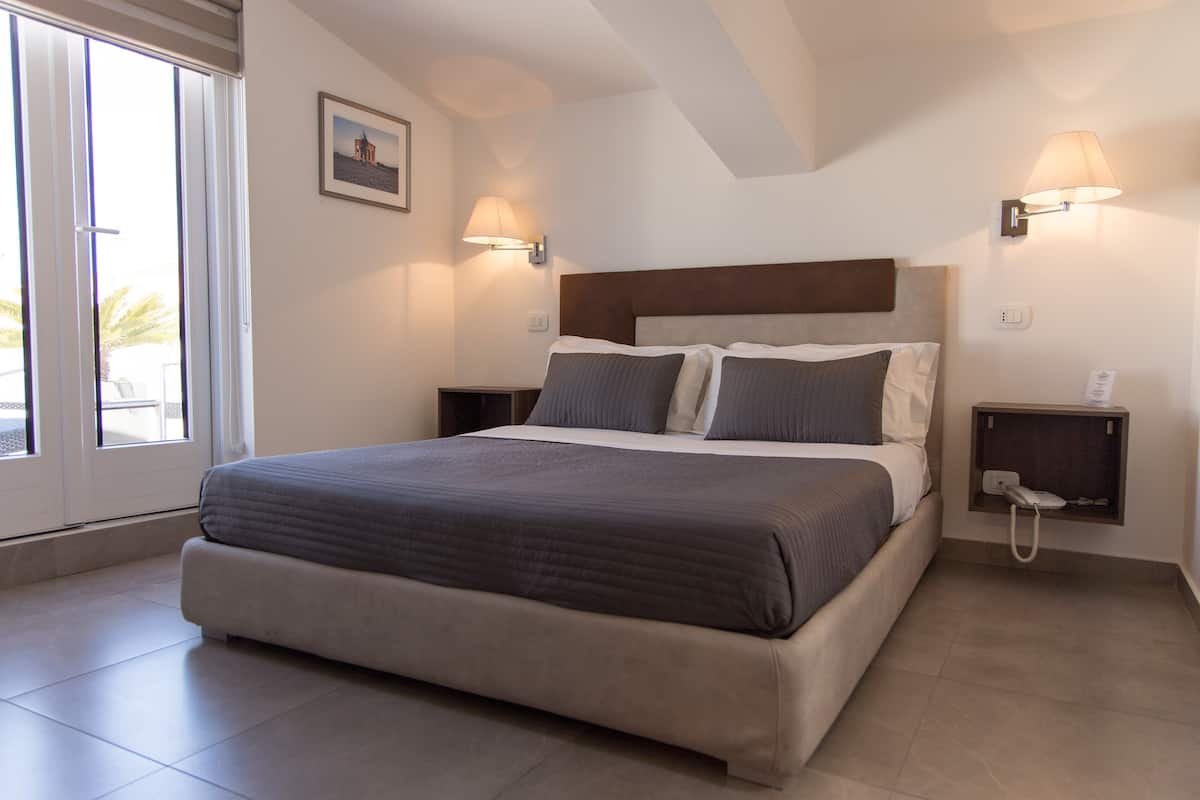 A modern bedroom with a large bed, two bedside tables, and a nightstand with a phone.