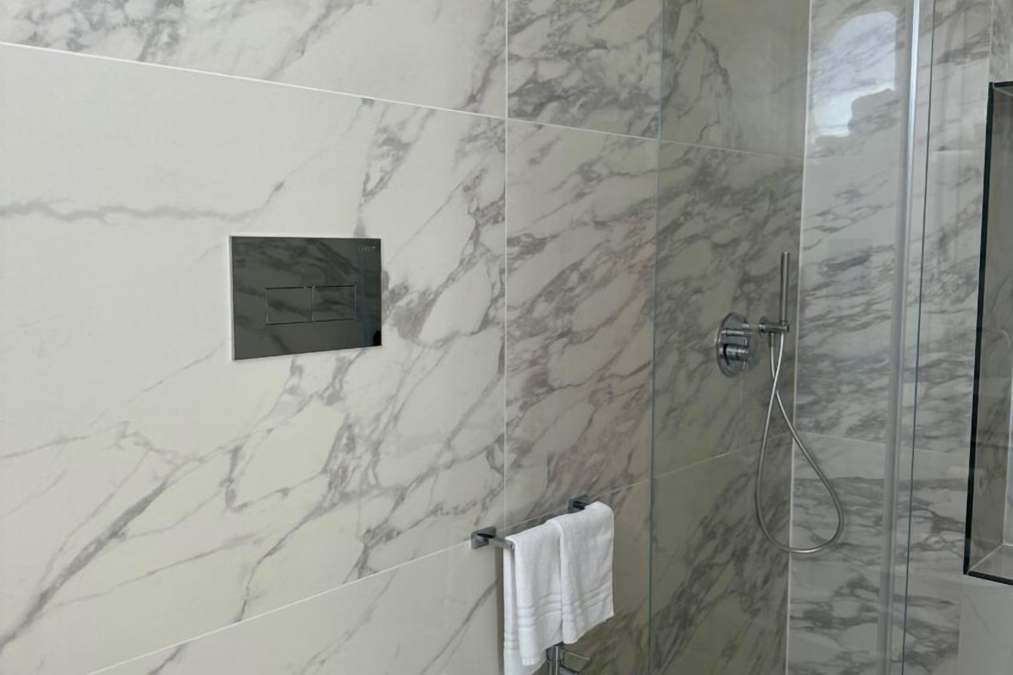 A modern bathroom with marble walls, a glass shower enclosure, and a towel rack.