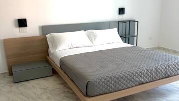 Quarto moderno com design minimalista, apresentando uma cama com colchão acolchoado cinza, cabeceira de madeira e móvel de armazenamento cinza sob a cama.