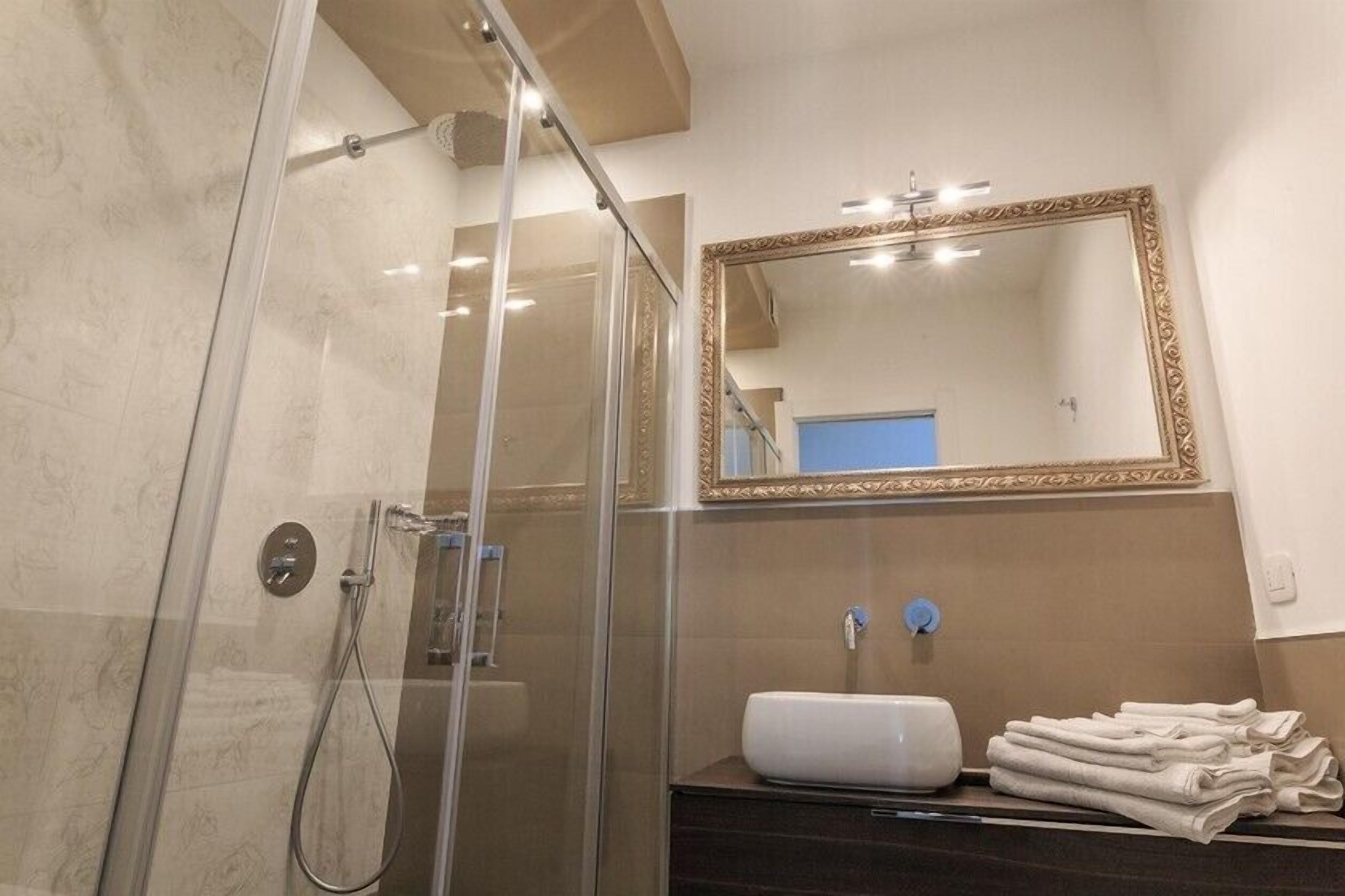 A modern bathroom with a glass-enclosed shower, a large mirror with a decorative frame, and a dark wooden vanity with a white sink and towels.