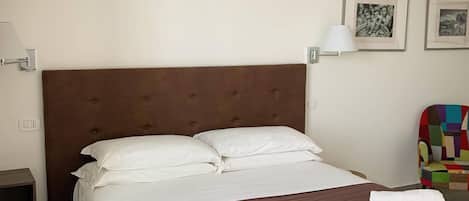 Hotelkamer met een groot bed, witte kussens, een bruin hoofdbord, een nachtkastje, een lamp en twee ingelijste foto's aan de muur.