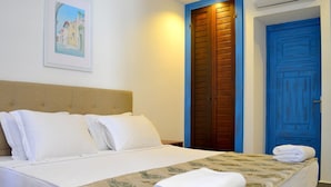Un lit bien fait, avec du linge de lit blanc et une couvre-lit à motifs floraux, une tête de lit en bois et une porte bleue en arrière-plan.