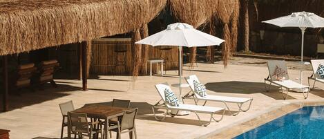 A pool area with lounge chairs, a table, and umbrellas.