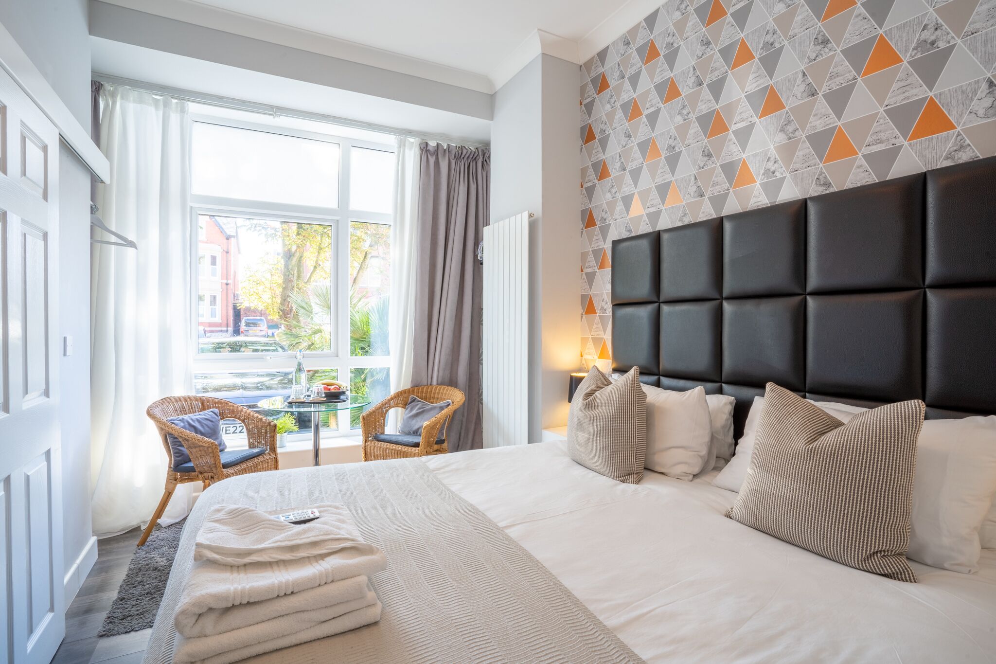 A hotel room with a large bed, a view of the outside, and a patterned wall.