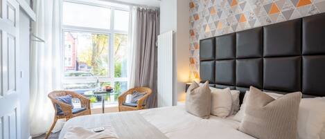 A hotel room with a large bed, a view of the outside, and a patterned wall.