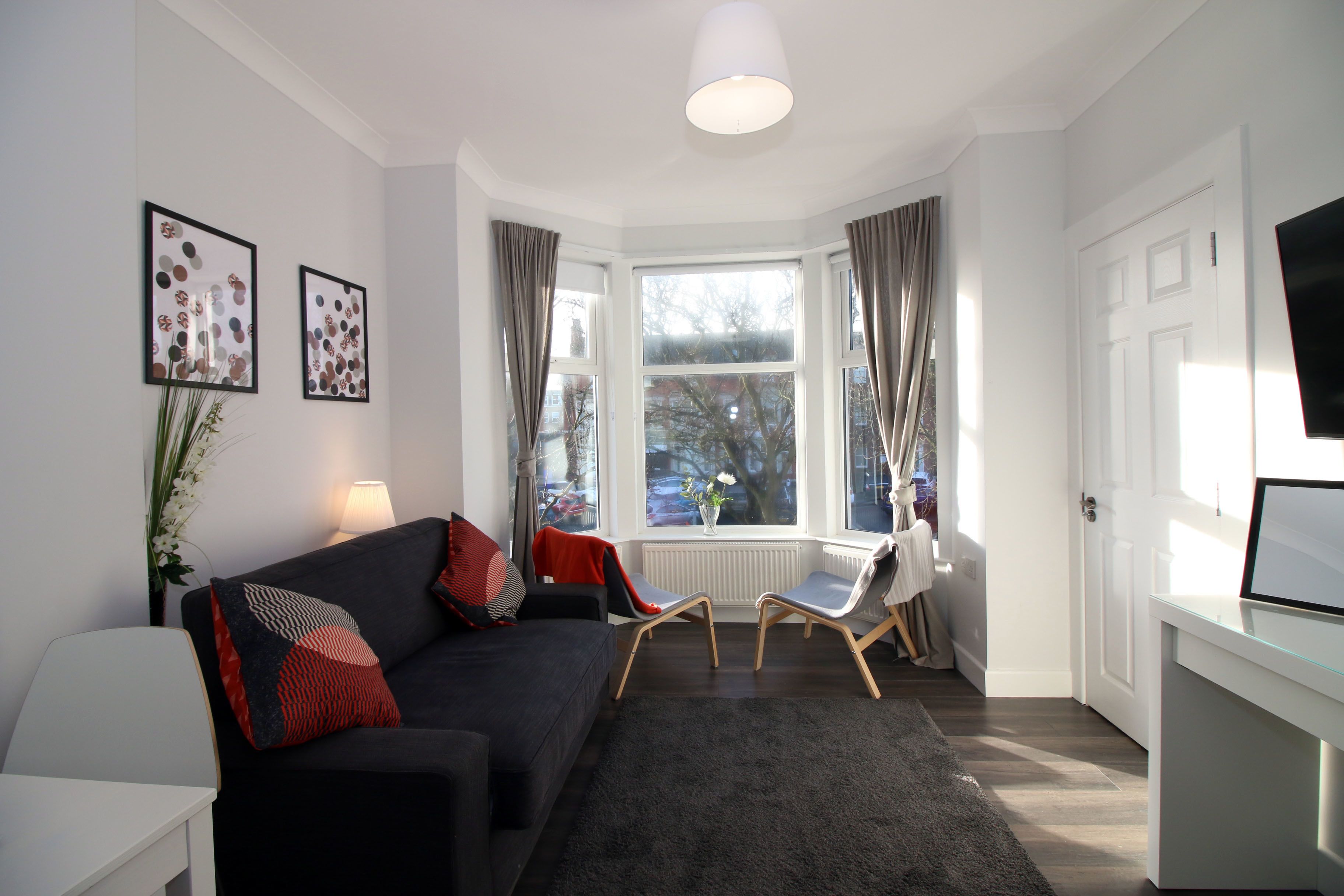 Een moderne woonkamer met een donkere bank, twee fauteuils, een wit bureau en een groot raam met gordijnen.