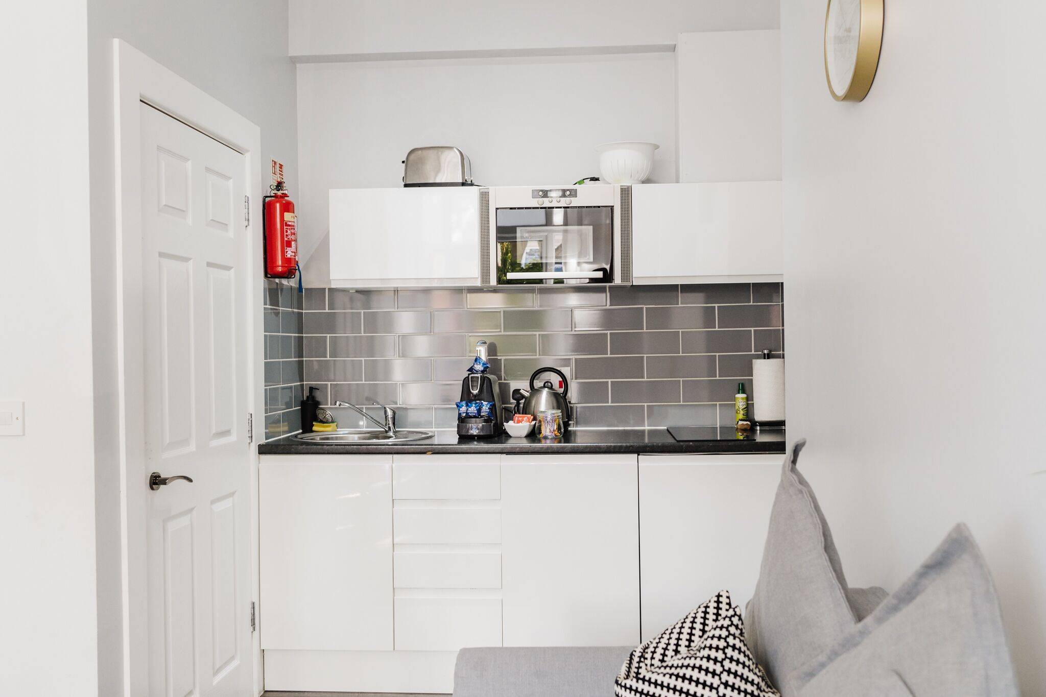 A compact kitchen with white cabinets, a microwave, a kettle, and a toaster.