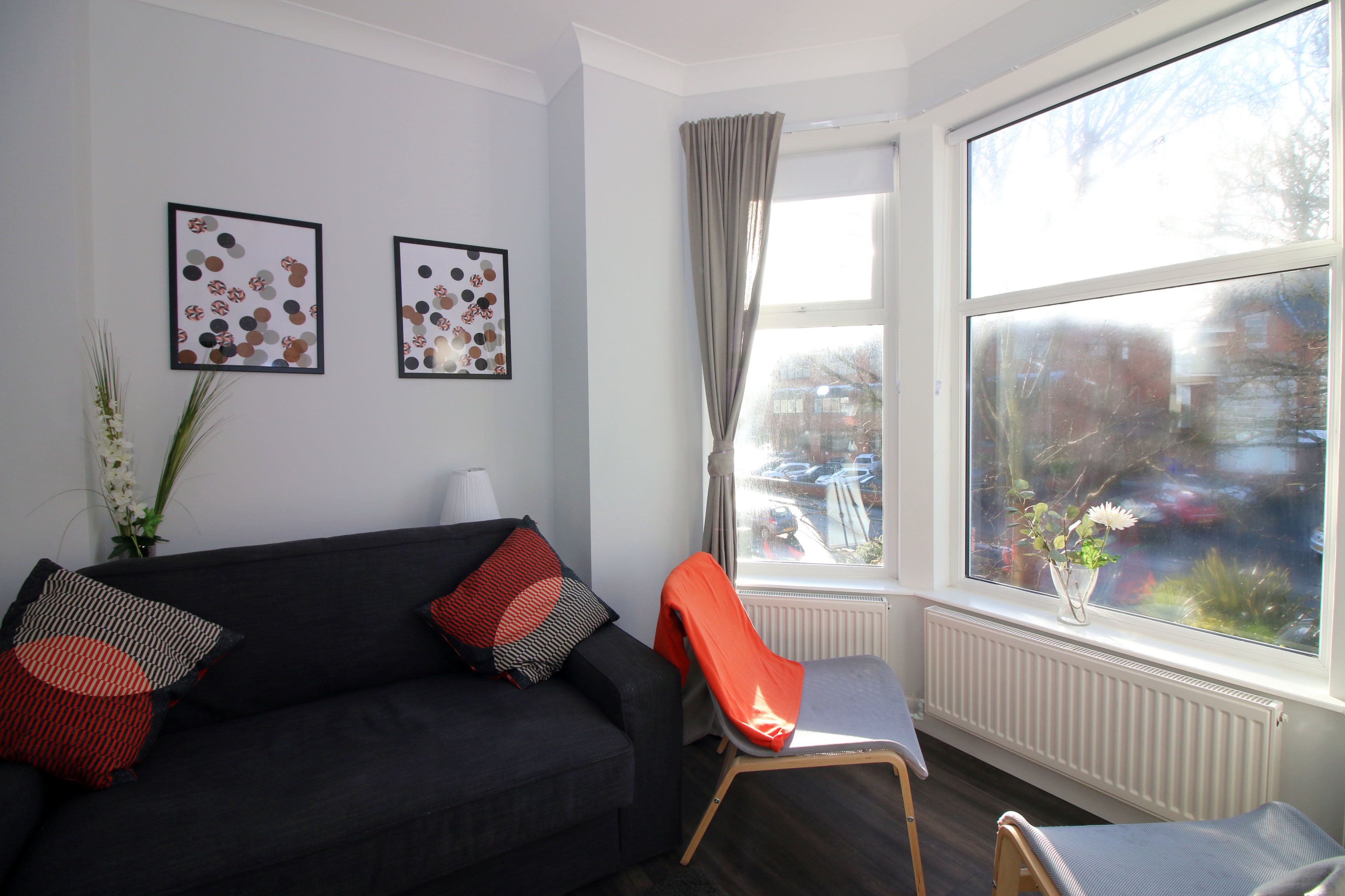 Een moderne woonkamer met een zwarte bank, een rode fauteuil en twee abstracte kunstwerken in lijsten aan de muur.