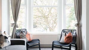 A modern living room with a large bay window, two black chairs with patterned cushions, a grey sofa, and a shaggy rug. - Sweet Suites Lytham St Annes (Lytham St. Anne's)