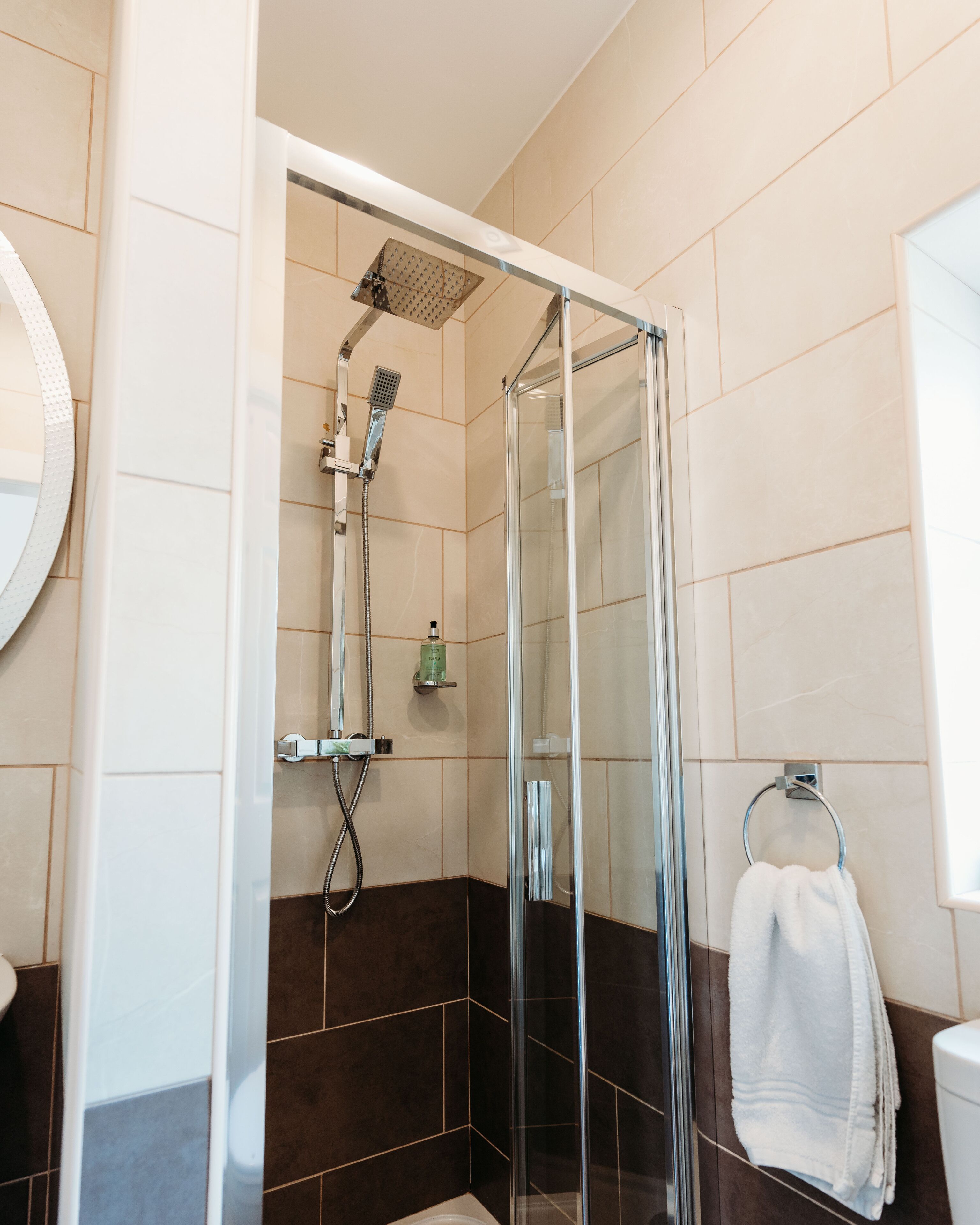 A glass-enclosed shower with a handheld showerhead and a wall-mounted faucet.