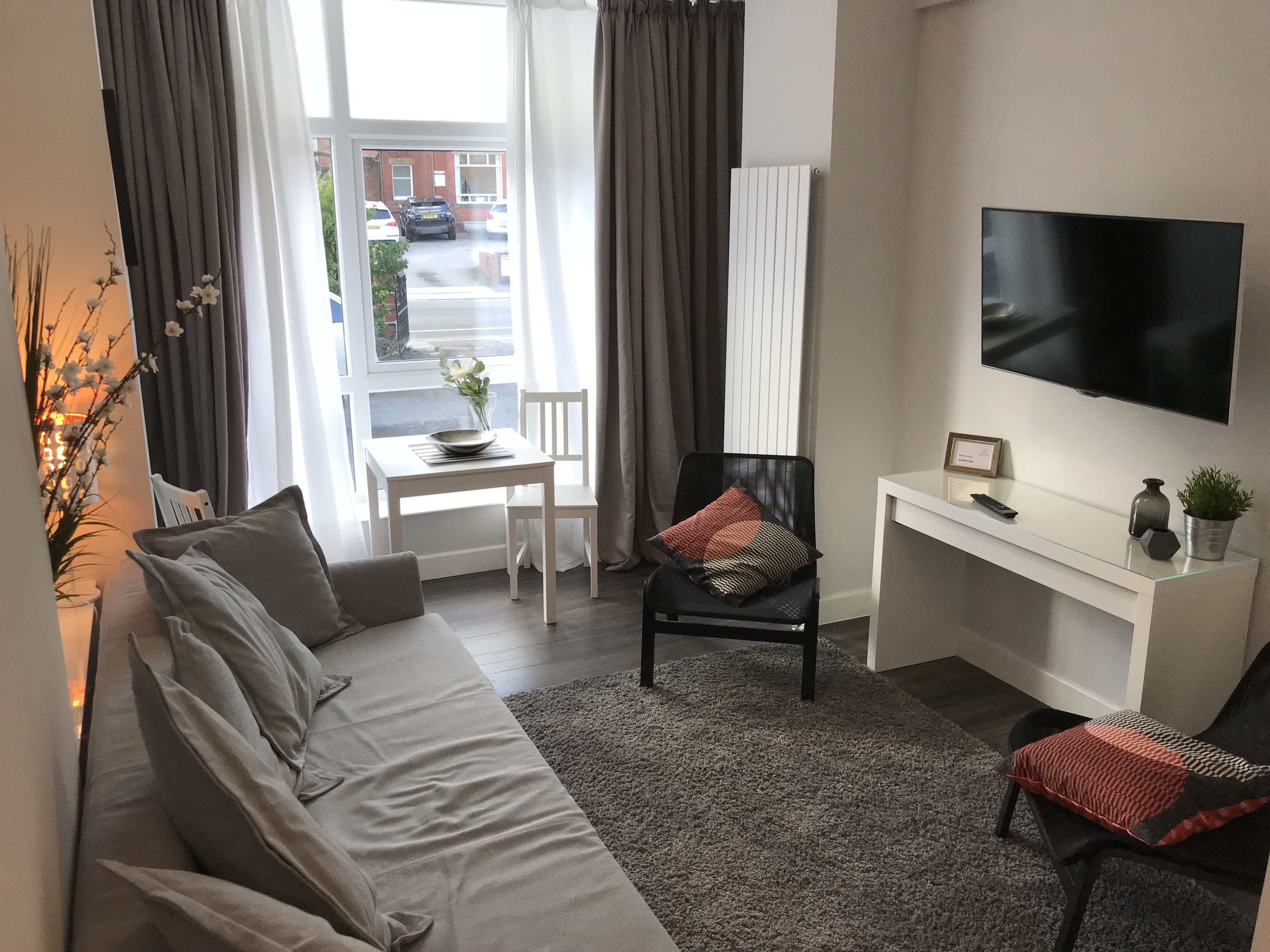 A modern living room with a sofa, a dining table, a chair, a TV, and a small desk.