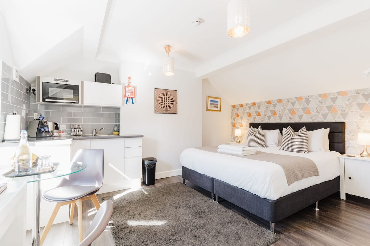 Ein modernes Schlafzimmer mit einem großen Bett, Nachttischen und einer kleinen Küchenzeile.