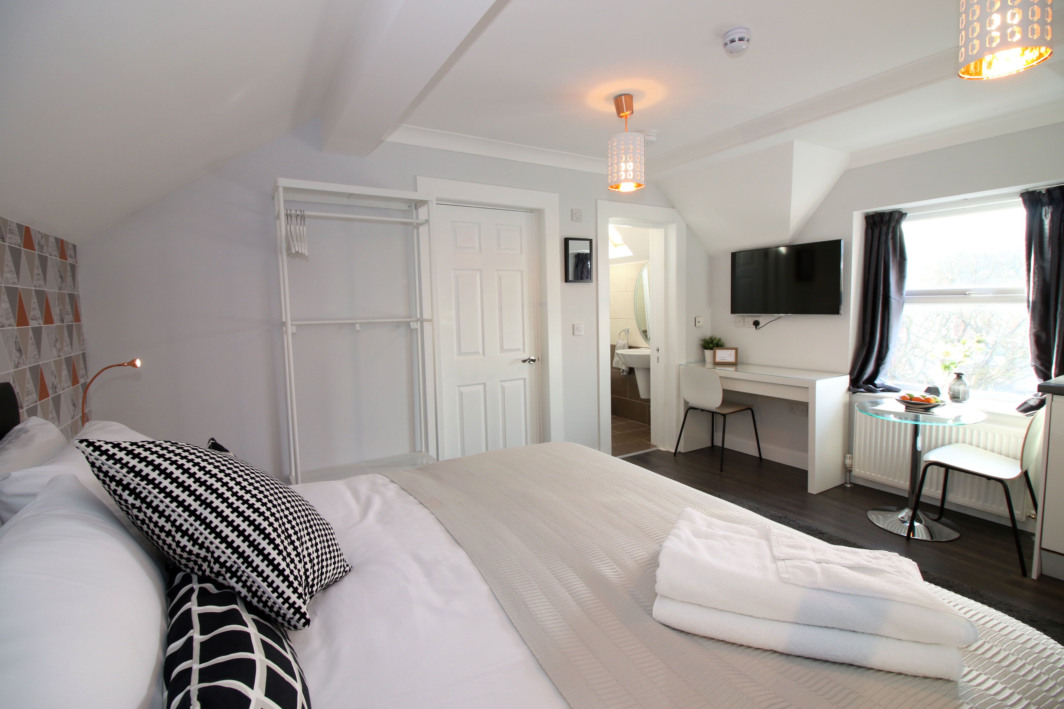 A hotel room with a bed, a desk, a chair, a TV, and a window with curtains.