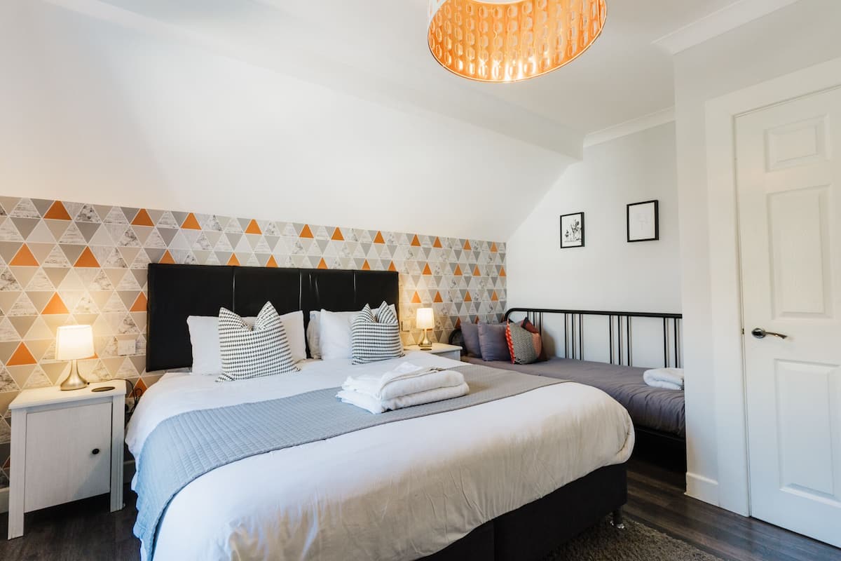 Ein modernes Hotelzimmer mit einem großen Bett, einem kleineren Bett, einem Nachttisch mit Lampe und einer Tür.