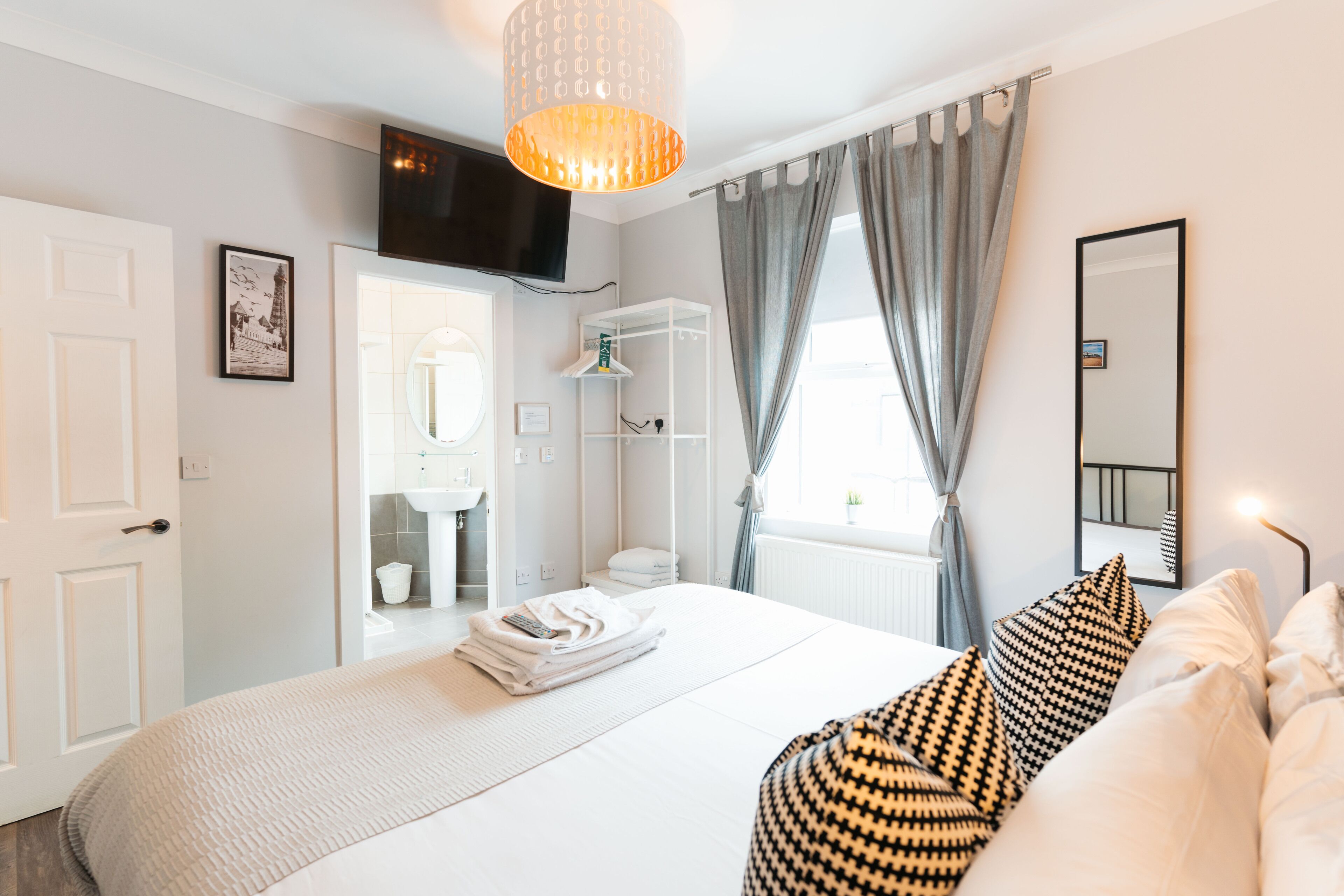 A modern hotel room with a large bed, a wardrobe, a television, and a bathroom visible through an open door.