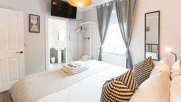 A modern hotel room with a large bed, a wardrobe, a television, and a bathroom visible through an open door.